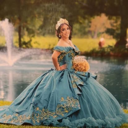 A woman in a blue ball gown is standing in front of a fountain.