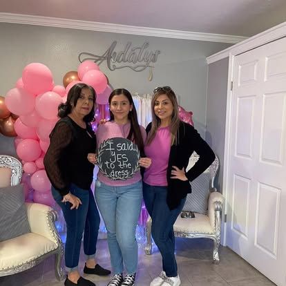 Three women are posing for a picture in a room with pink balloons.