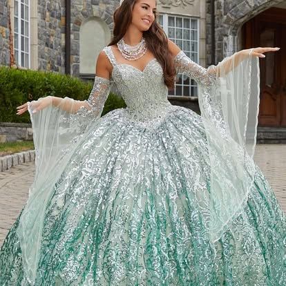 A woman in a green and silver ball gown is standing in front of a building.