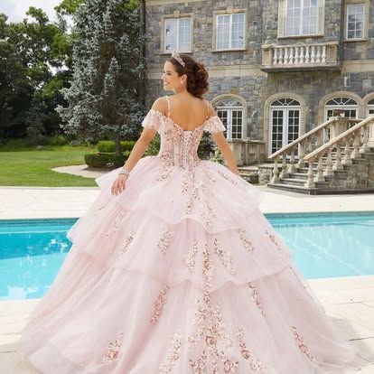 A woman in a pink ball gown is standing next to a pool.
