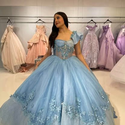 A woman in a blue ball gown is standing in front of a row of dresses.