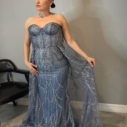 A woman in a blue strapless dress is standing in front of a chair.