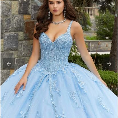 A woman in a light blue ball gown is standing in front of a brick wall.