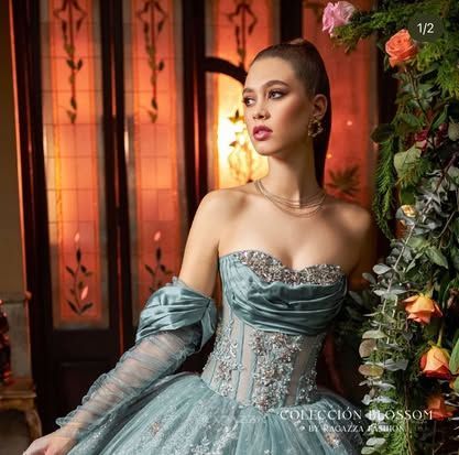 A woman in a blue ball gown is standing in front of flowers.