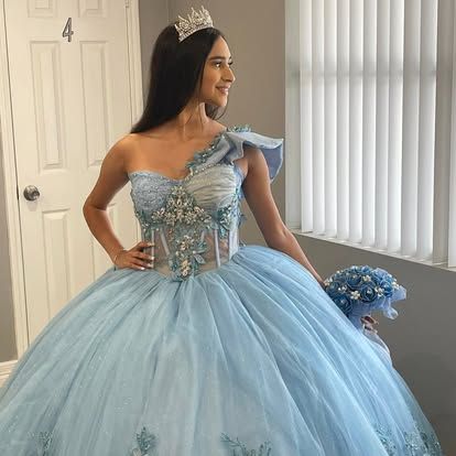 A woman is wearing a light blue ball gown and holding a bouquet of flowers.