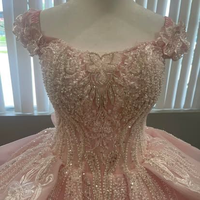 A pink ball gown is on a mannequin in front of a window.