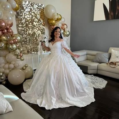 A woman in a wedding dress is standing in a living room holding a bouquet of balloons.