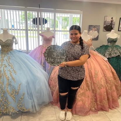 A woman is standing in front of a bunch of dresses holding a sign.
