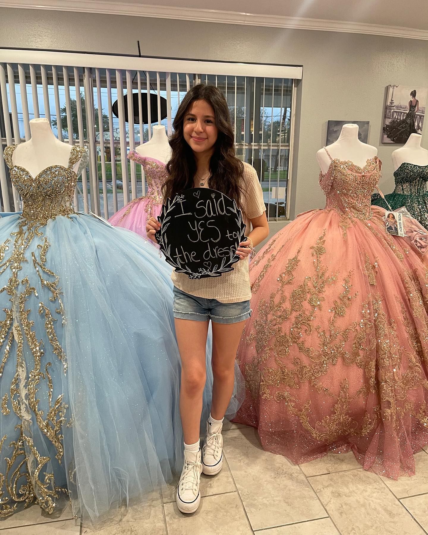A woman is standing in front of a bunch of dresses holding a sign.