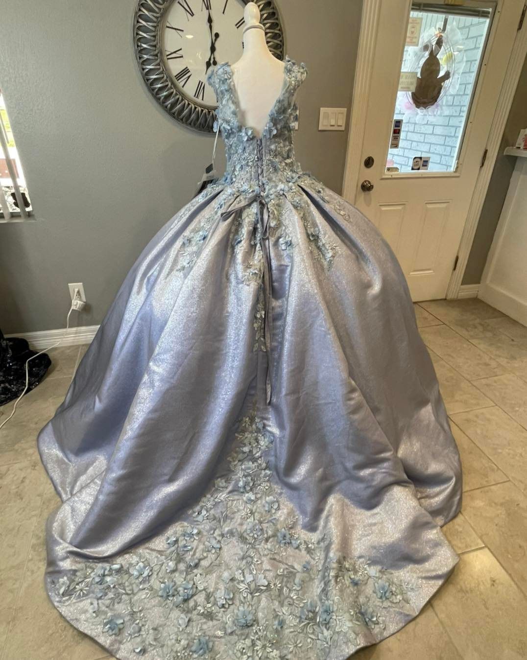 A blue ball gown is on a mannequin in front of a clock.