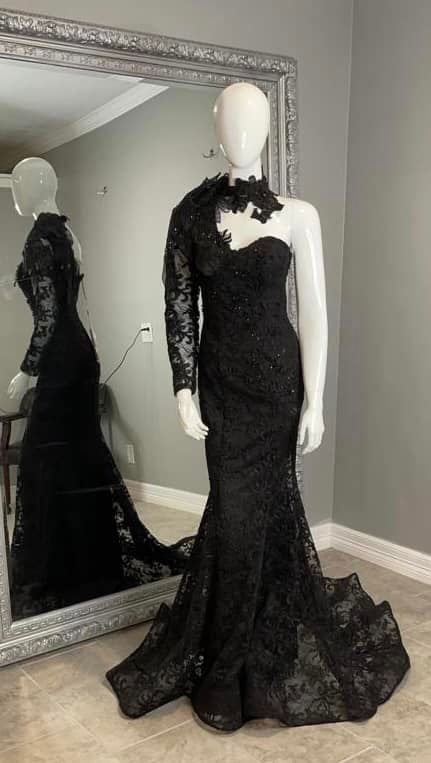 A black lace dress is on a mannequin in front of a mirror.