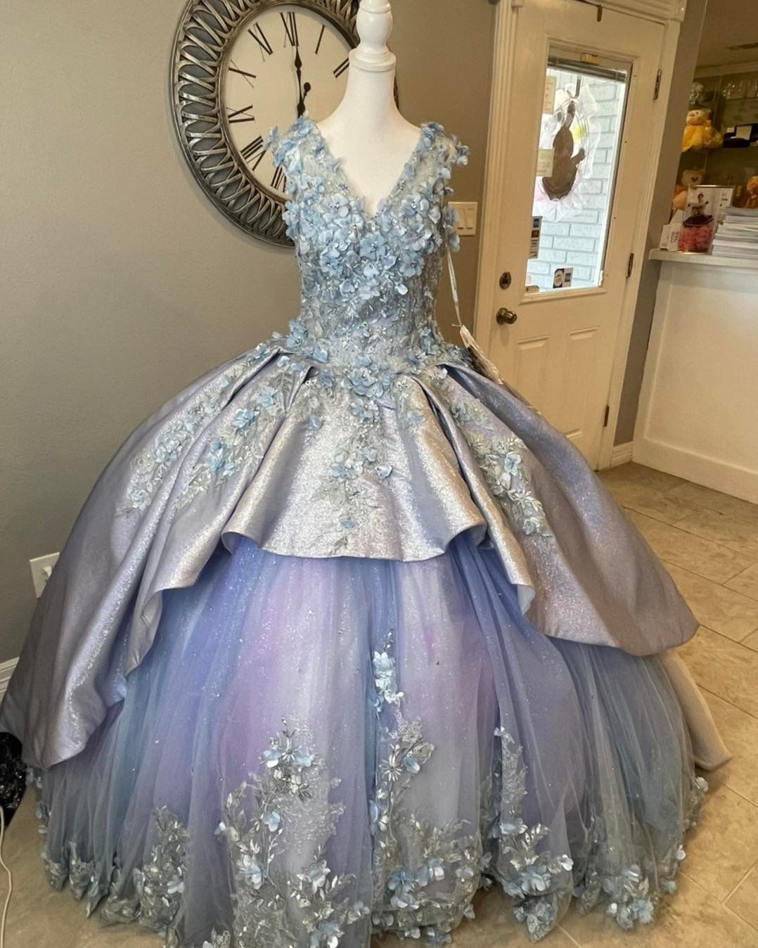 A ball gown is on a mannequin in front of a clock.