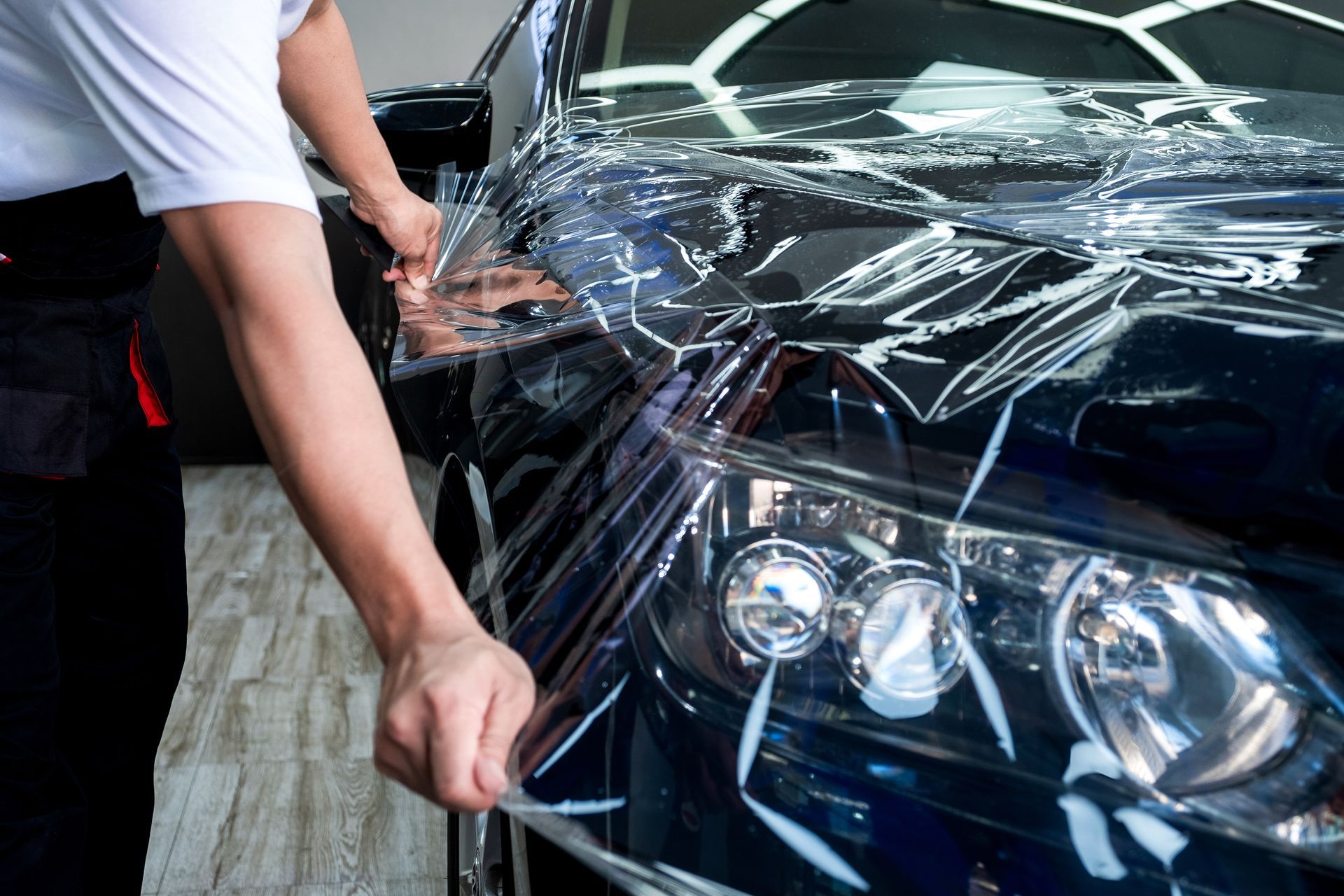 Person applying clear protective film to a car's headlight.