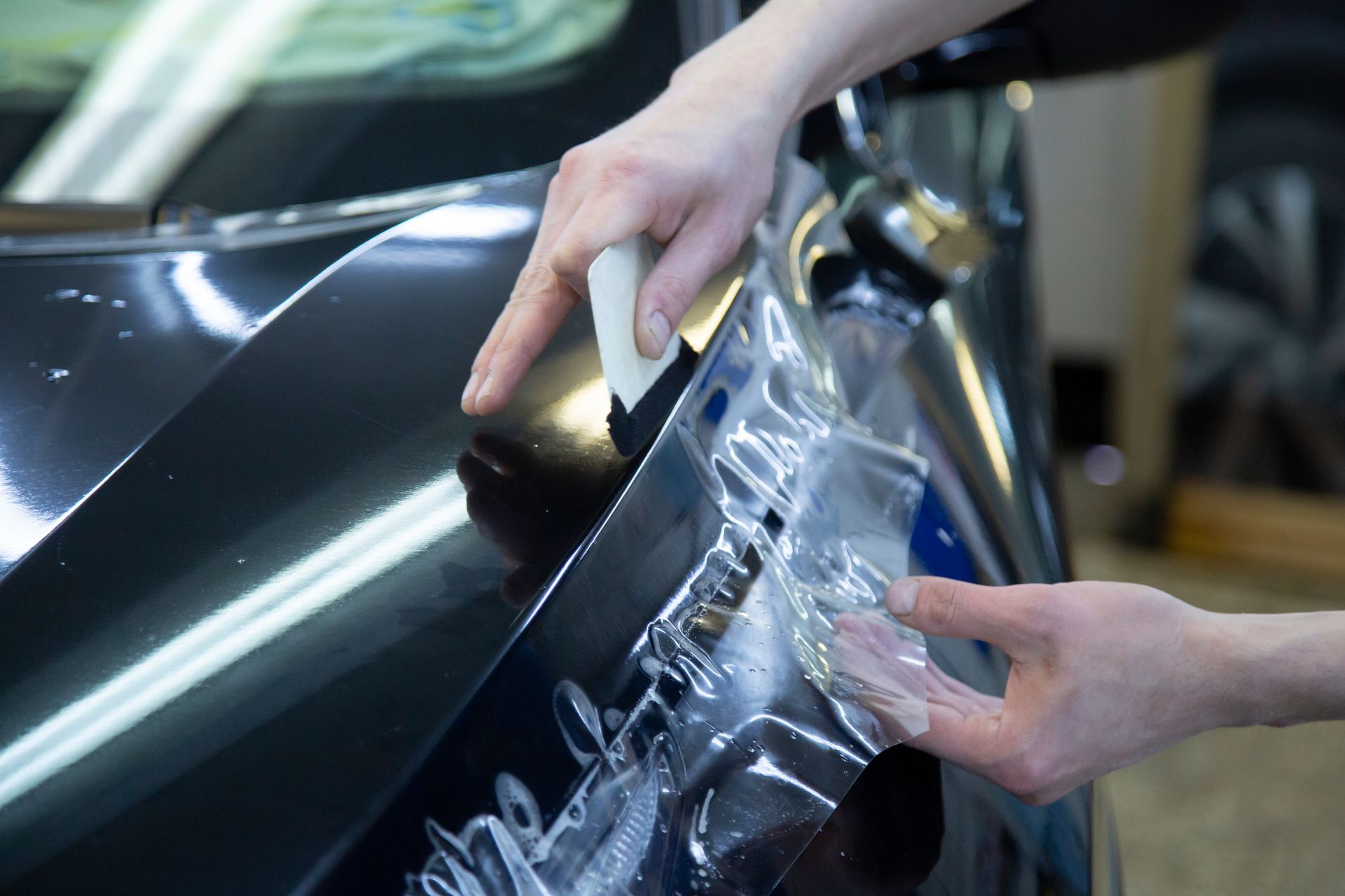 Person applying protective film to a black car's hood, using a squeegee.