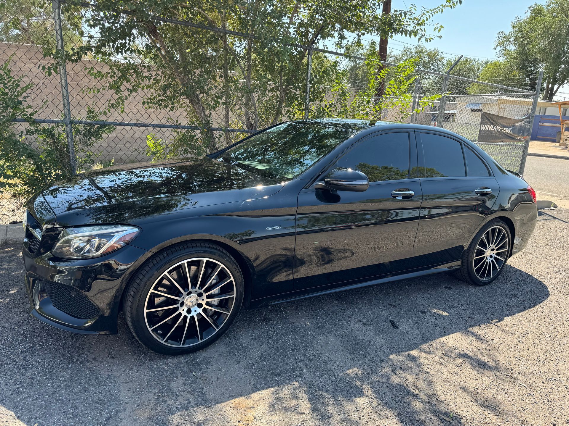 Black Mercedes sedan with tinted windows parked on gravel.