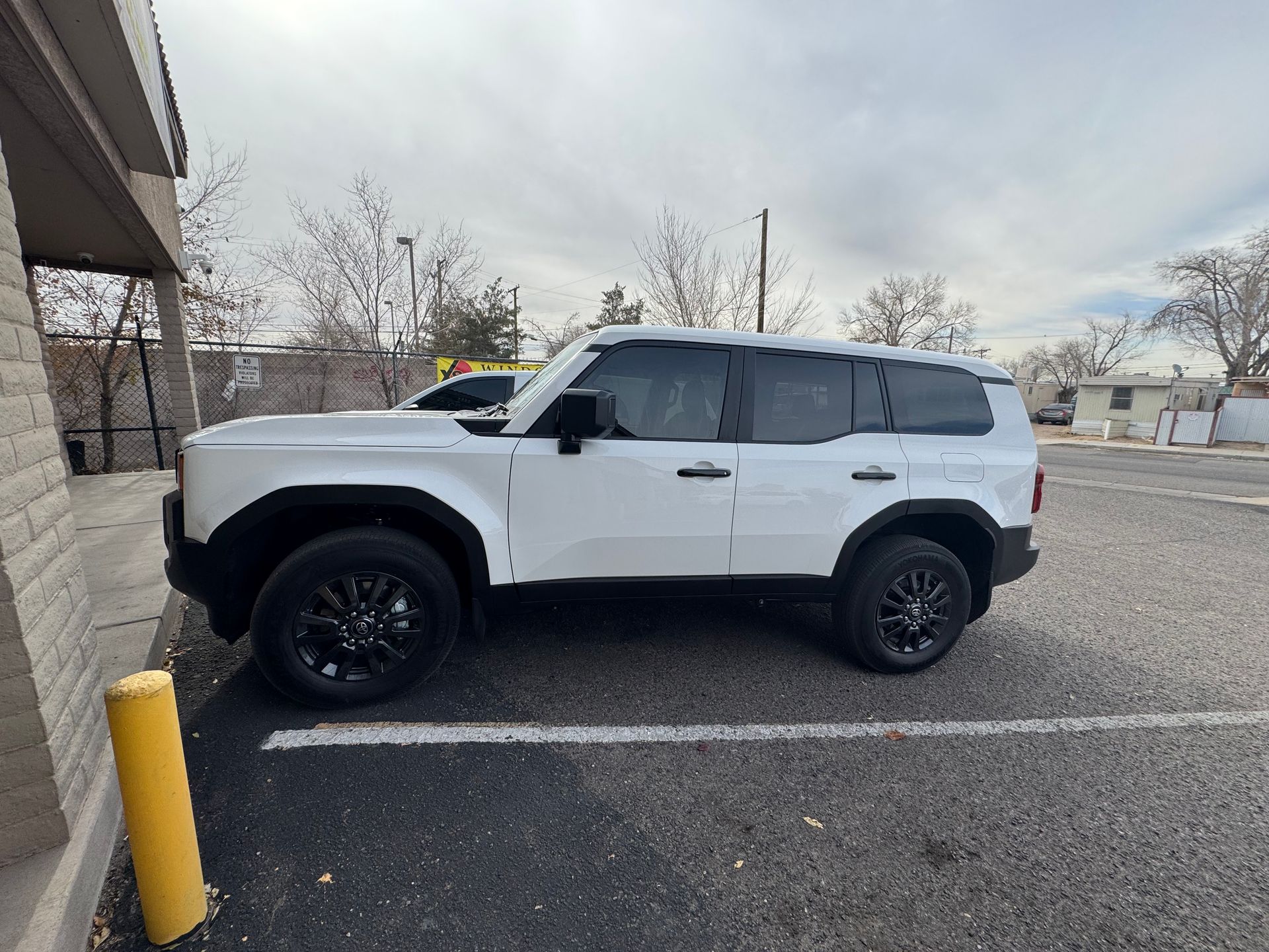 White Ford Bronco SUV parked on a paved lot next to a building, black wheels, overcast sky.