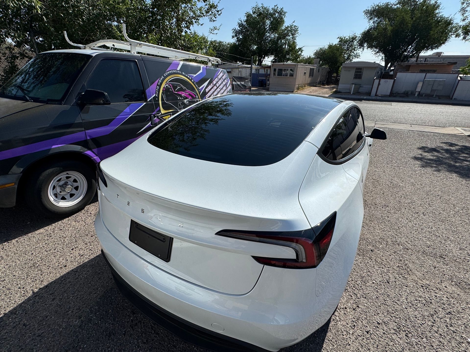 White Tesla car parked next to a dark van on a sunny day.