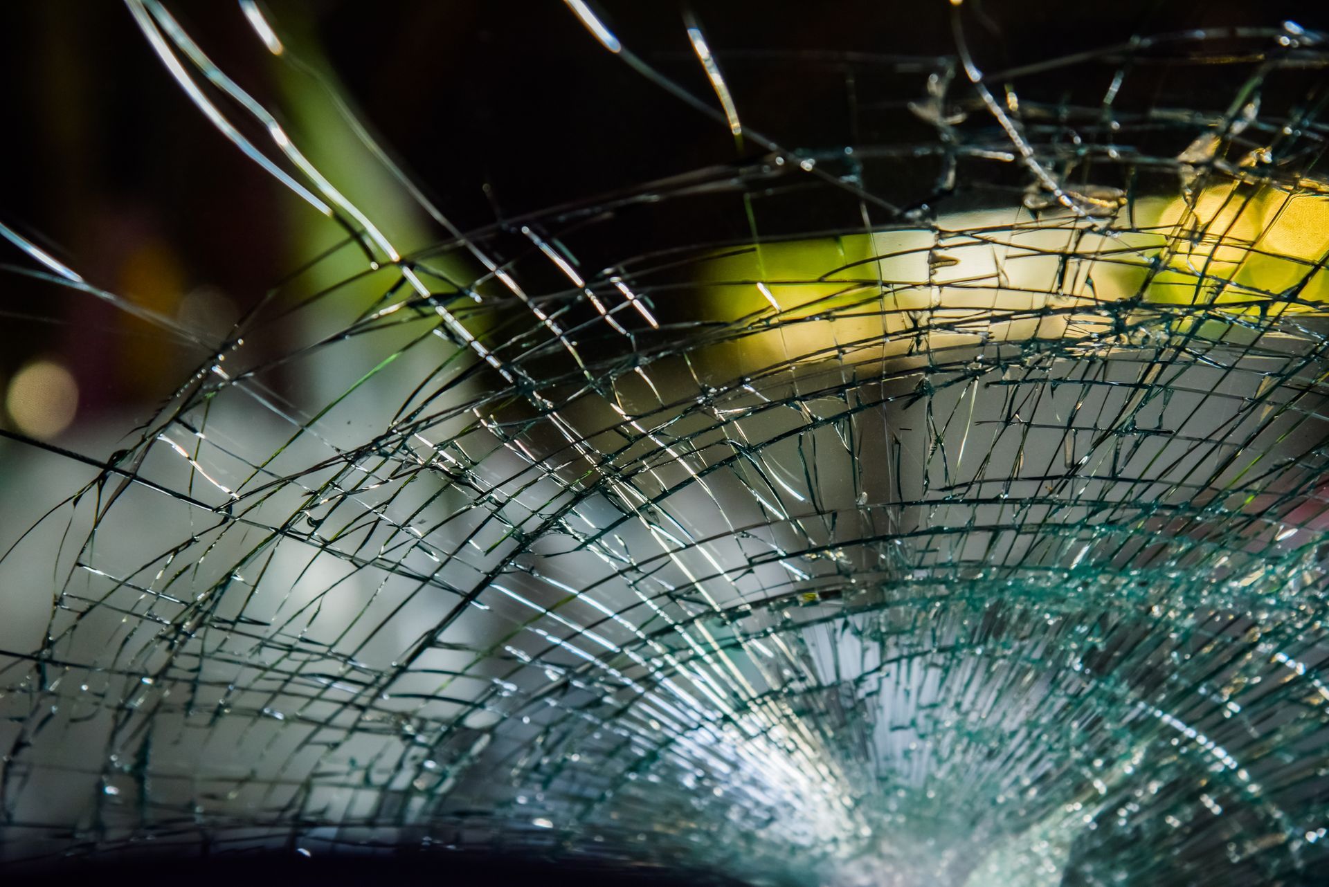Shattered car windshield, cracked glass, reflecting light, blurred background.