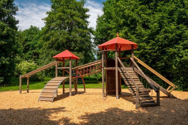 A wooden playground with a red umbrella in a park.