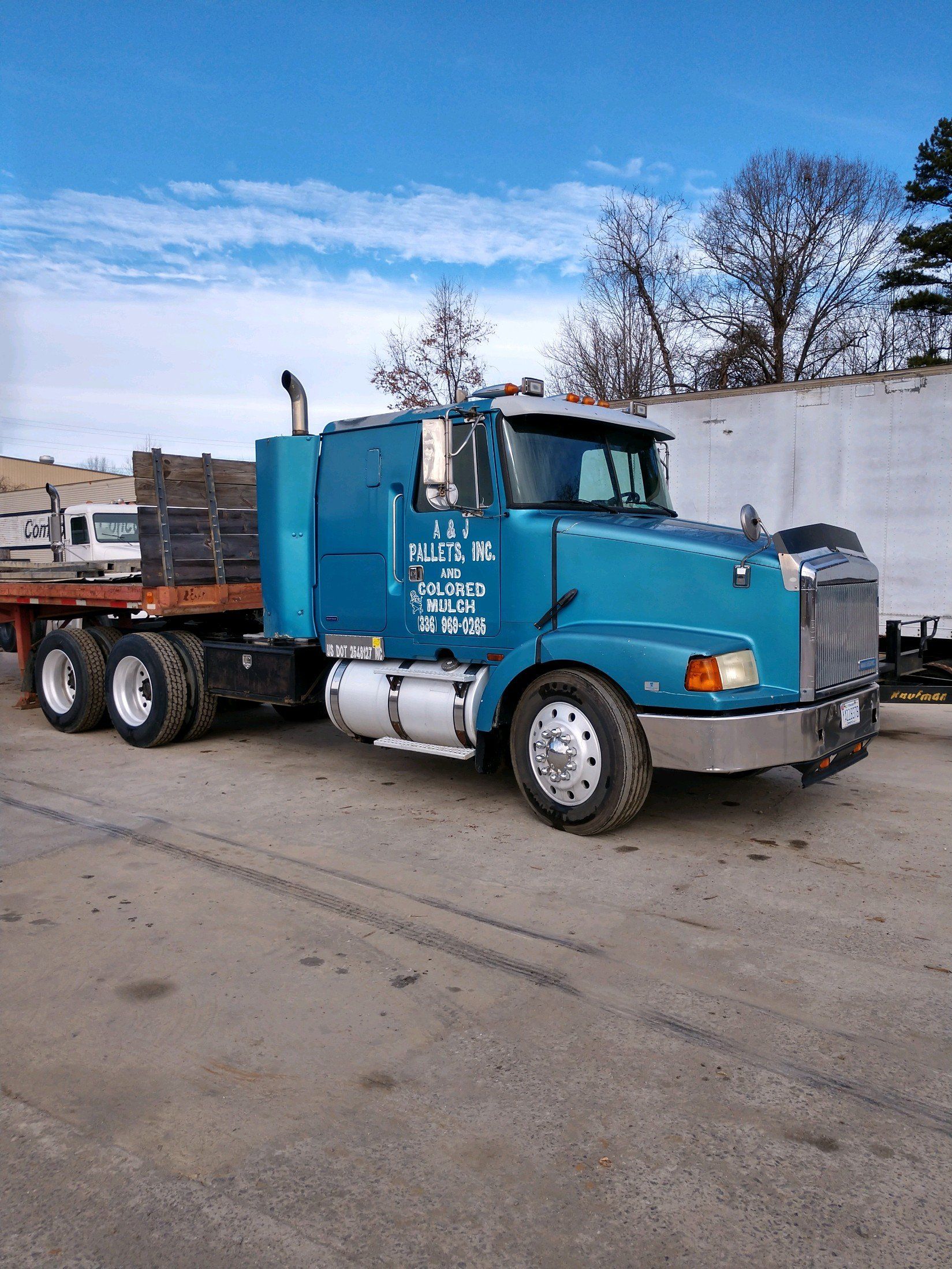 A blue semi truck with a flatbed trailer is parked in a parking lot.