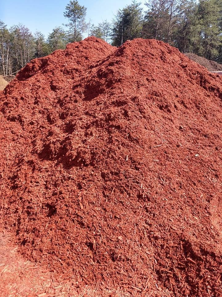 A large pile of red mulch is sitting on top of a dirt field.