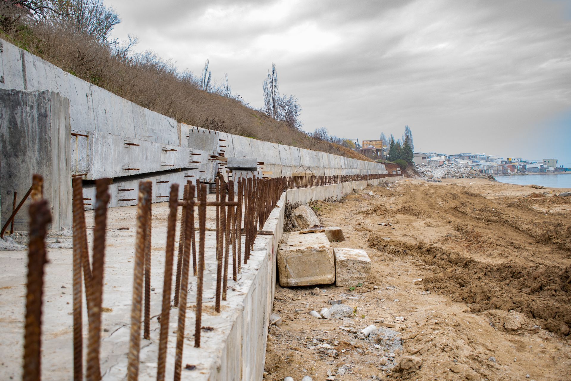 Concrete seawall under construction along a sandy beach under a cloudy sky.