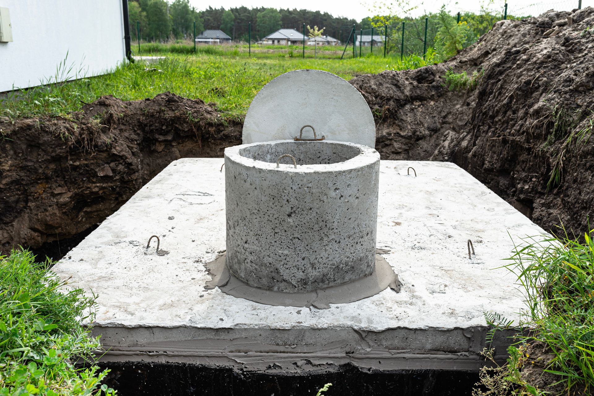 Concrete septic tank, partially buried in a yard, with lid and access opening.