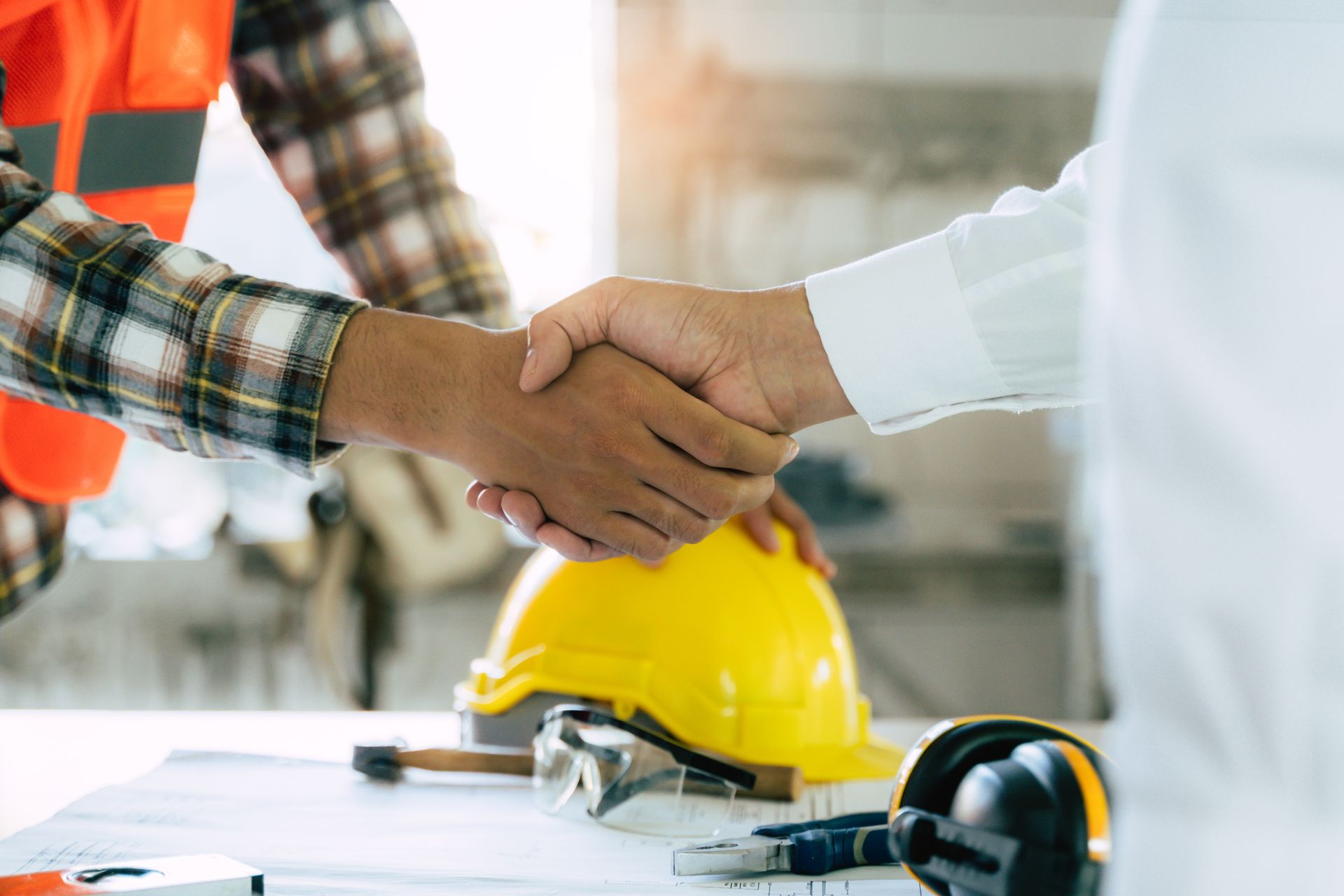 Two men shaking hands at a construction site, yellow hard hat and tools on a table.