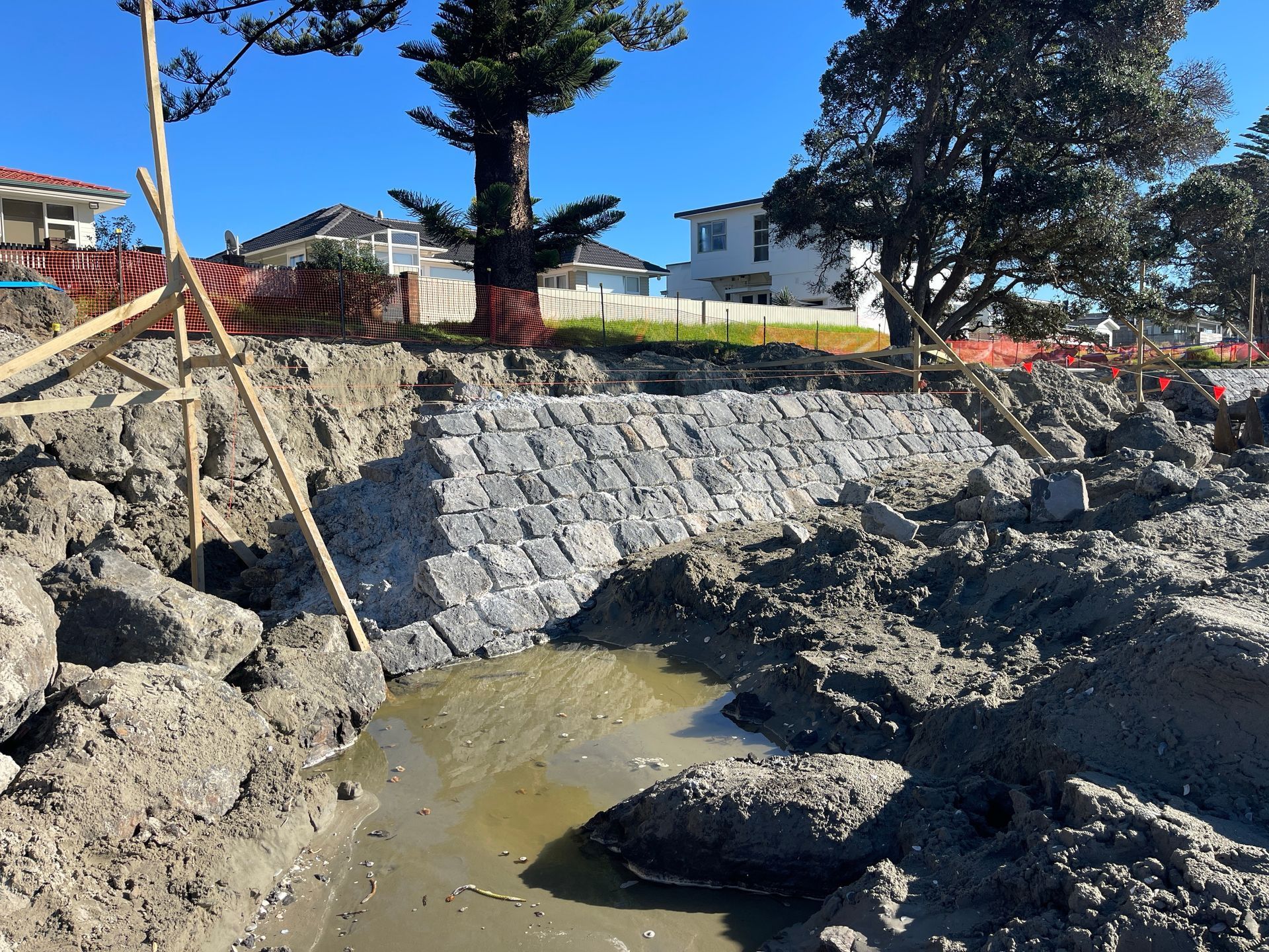 A newly constructed stone retaining wall on a muddy shoreline, houses in the background.