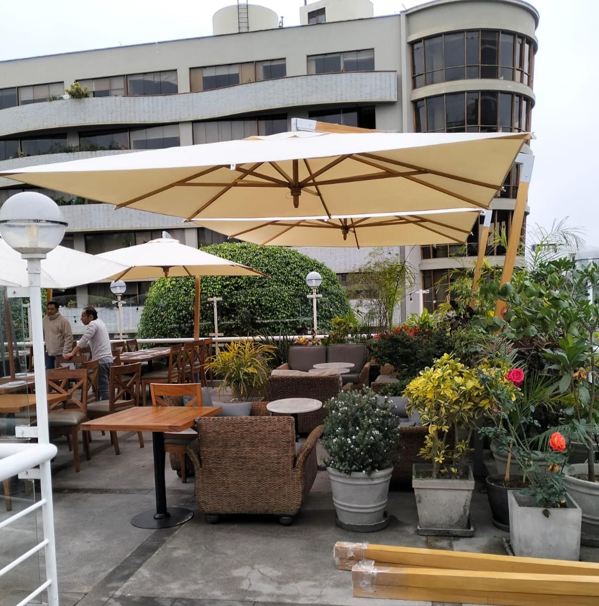 Restaurante al aire libre con sombrillas, mesas y plantas en la azotea. Hay gente.
