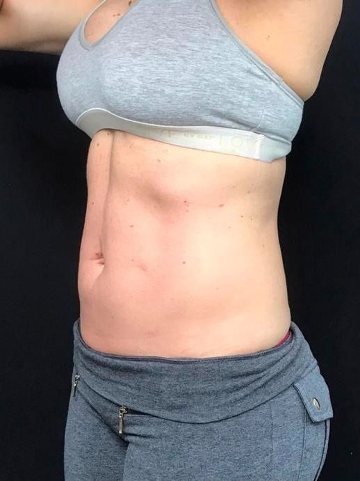 Woman in gray sports bra and pants, side view, showing abdomen. Black background.