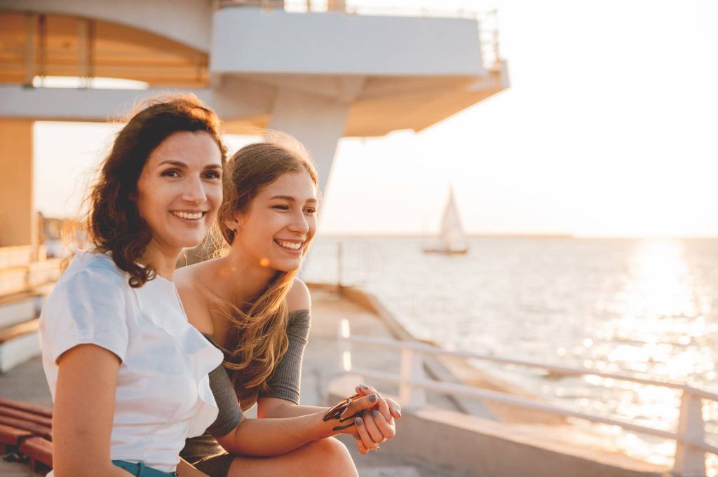 Two women are sitting on a bench near the ocean.