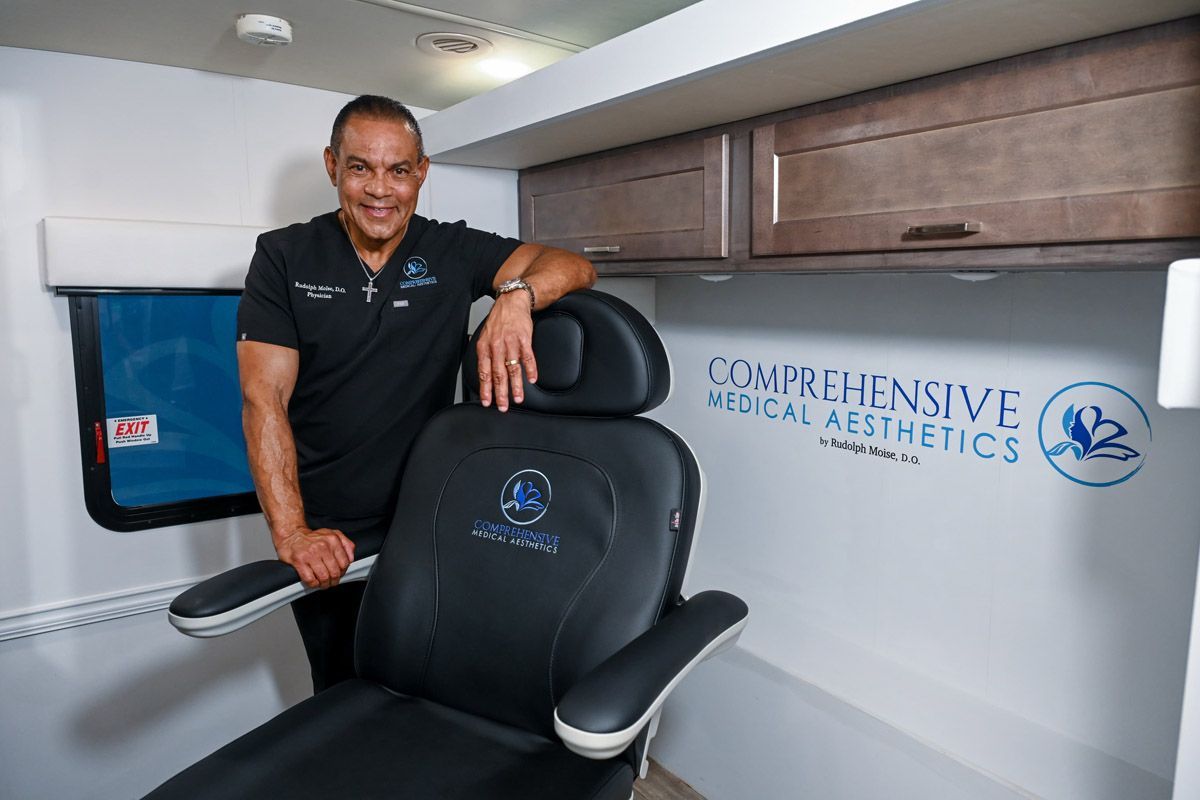 Man in medical scrubs stands next to a treatment chair inside a clinic, logo visible.