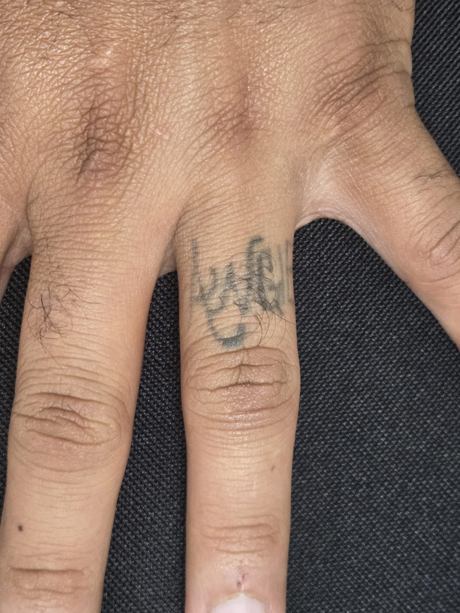 Close-up of a hand with a faded tattoo on the middle finger; the skin tone is light brown.