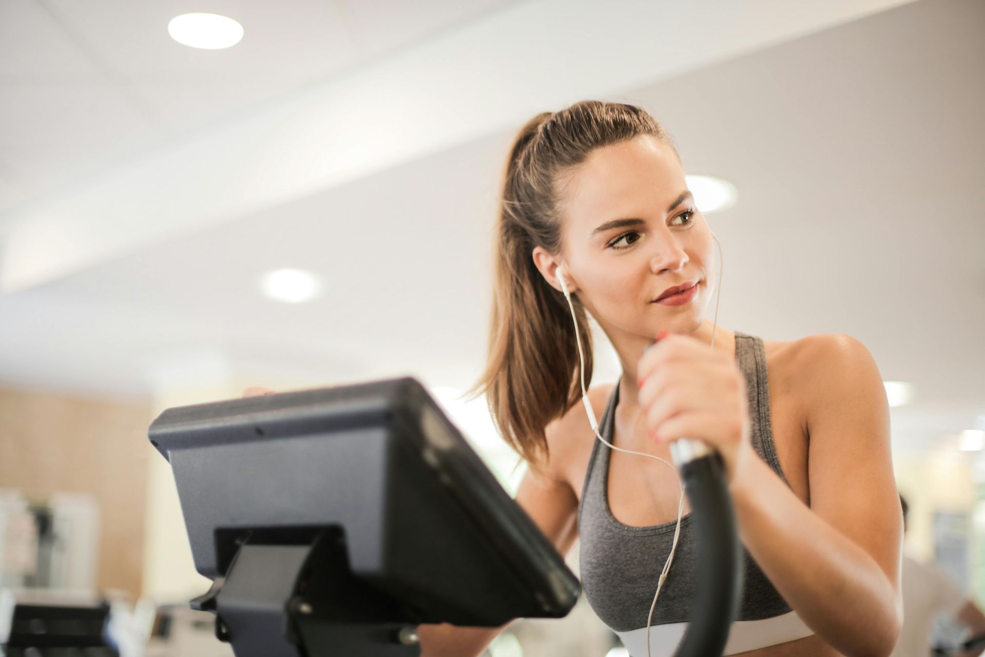 Woman in gym using elliptical machine, wearing earbuds and workout clothes.