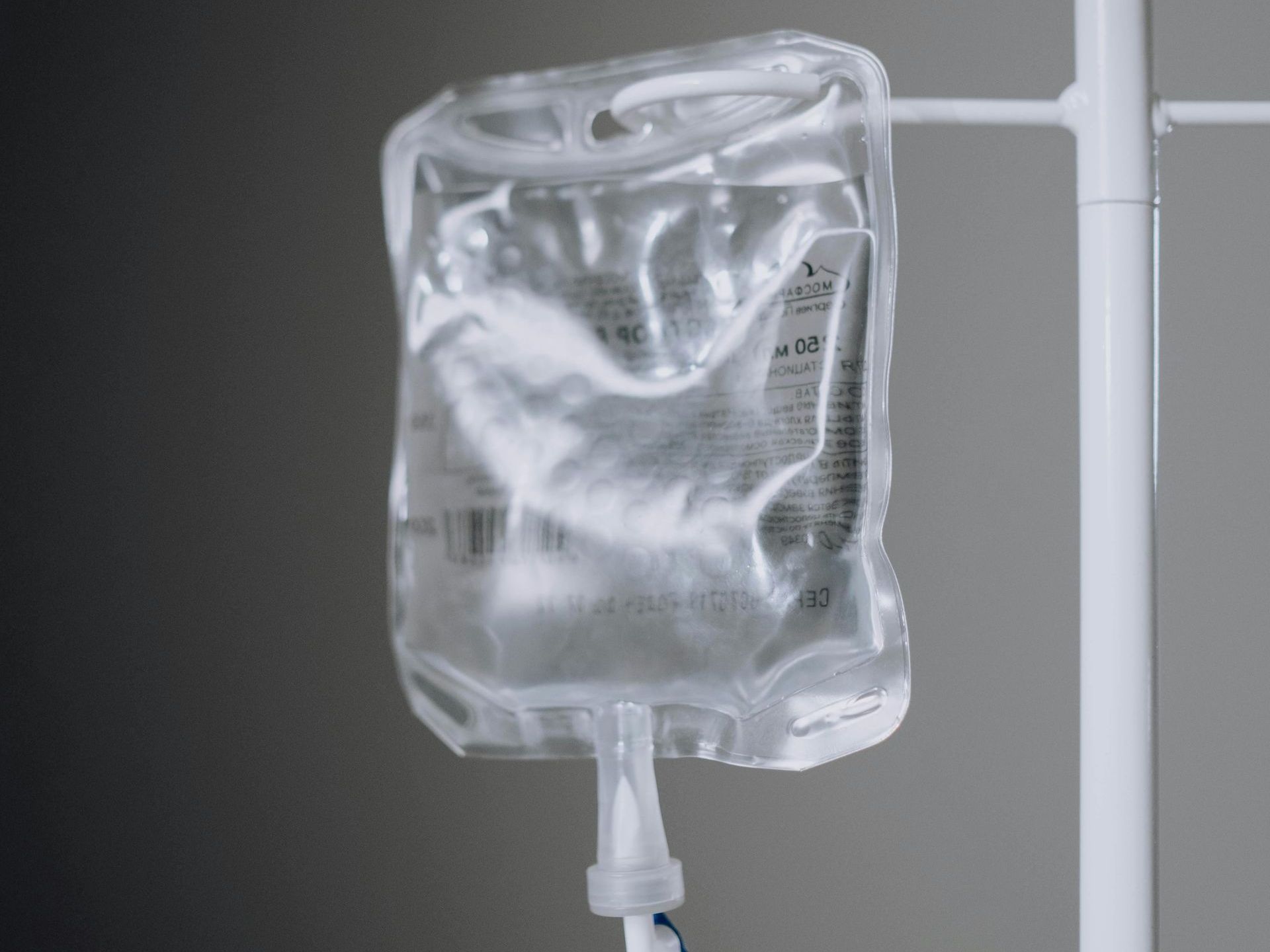 IV bag hanging on a white stand, containing clear liquid.