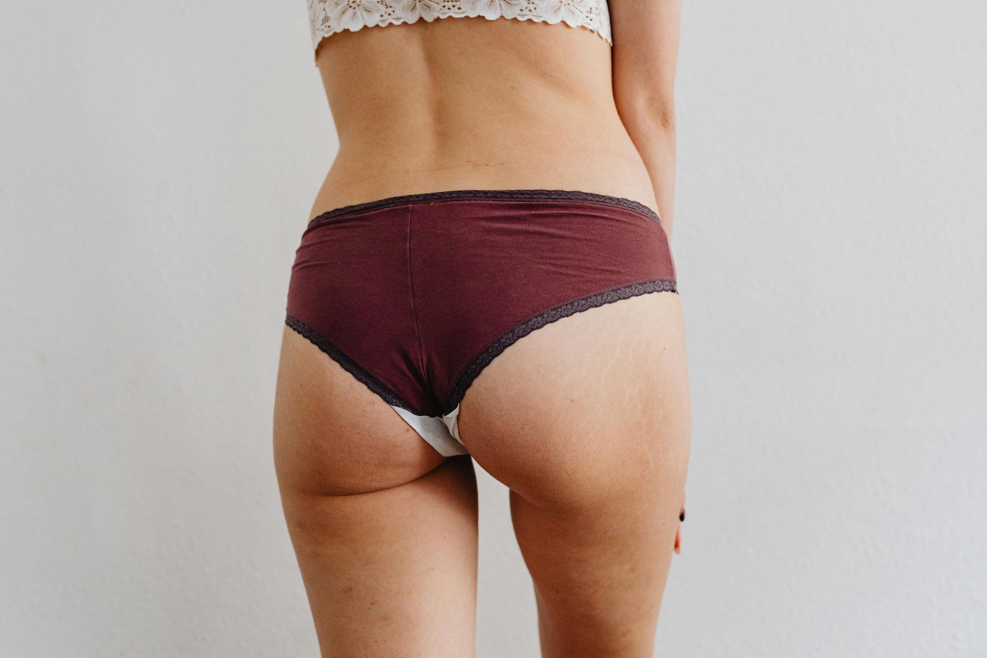 Person wearing maroon underwear standing against a white wall.