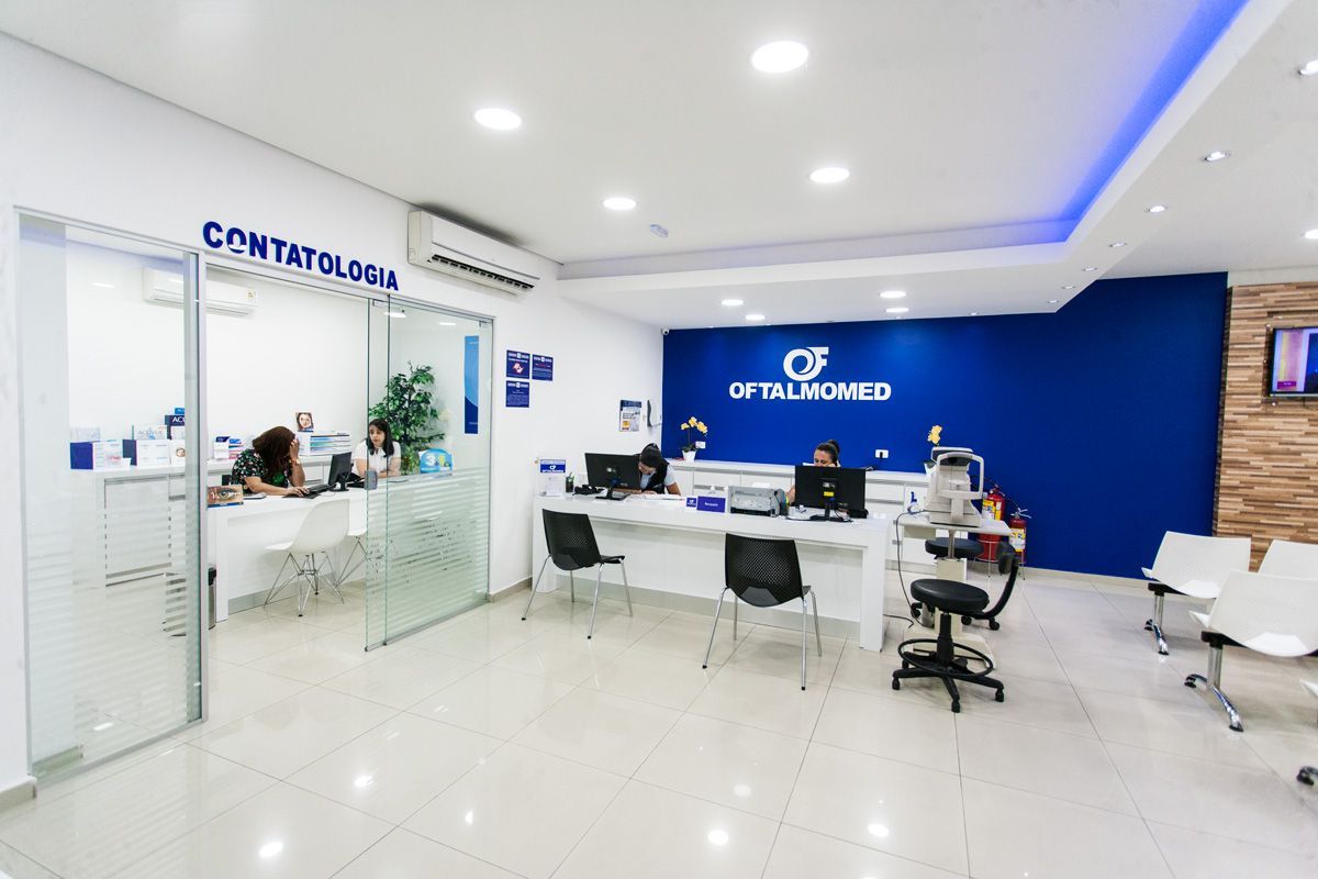 Um grupo de pessoas está sentado em mesas em uma sala com uma placa que diz contatologia