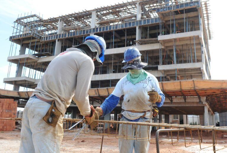 Dois trabalhadores da construção civil estão parados em frente a um prédio em construção.
