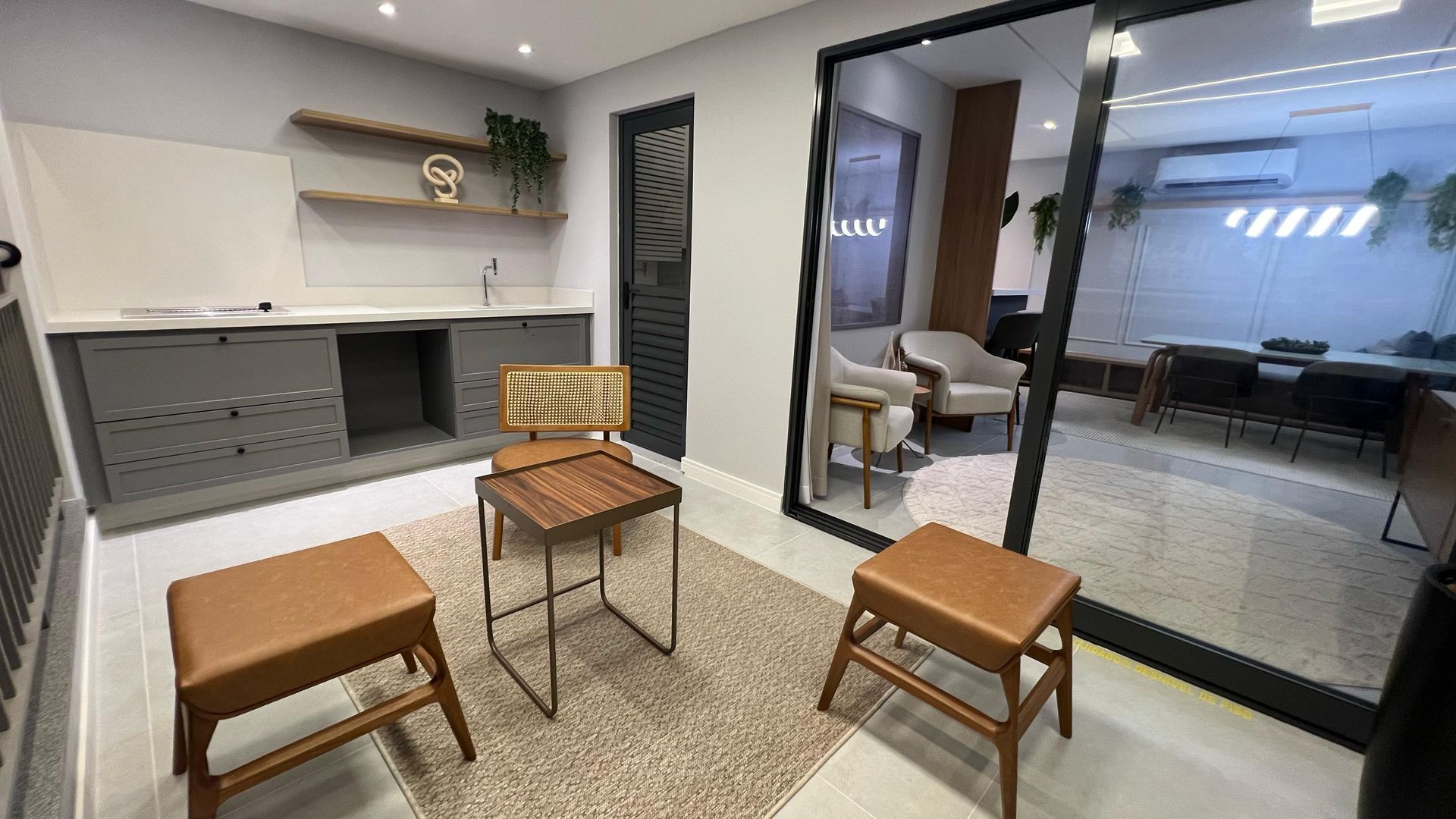 Sala de espera de escritório com armários cinza, prateleiras de madeira, cadeiras e um grande espelho que reflete outra sala.
