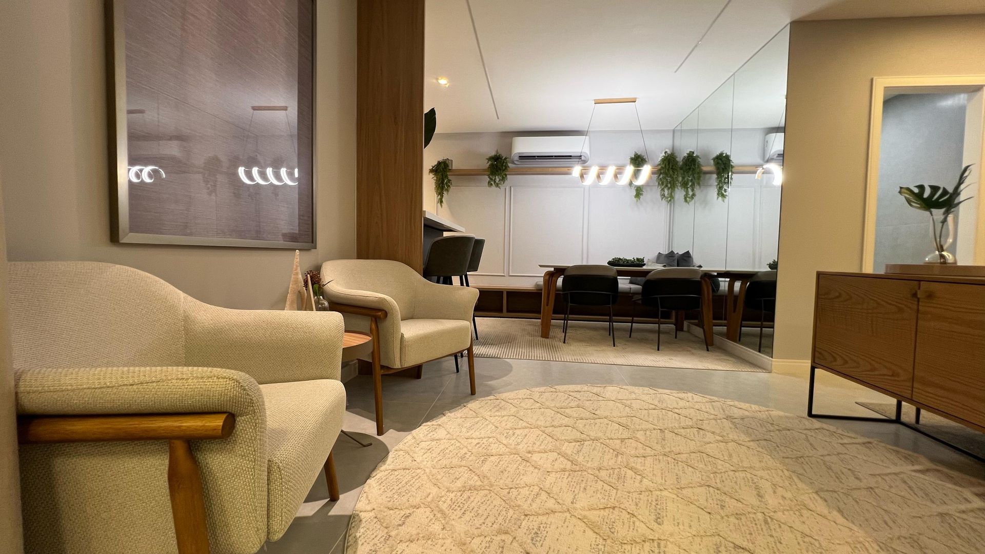 Sala de estar com duas poltronas brancas, um tapete grande e área de jantar com espelho.