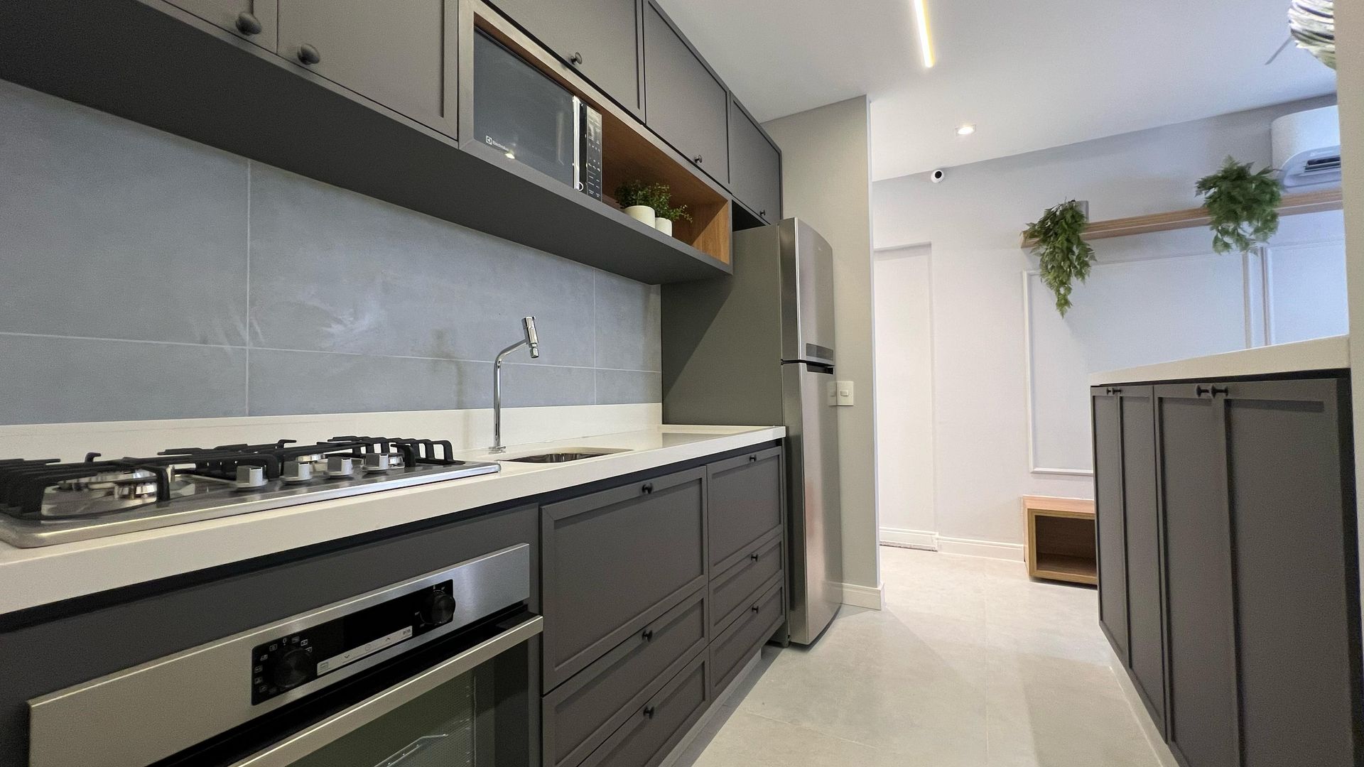 Cozinha moderna com armários cinza, bancadas brancas, eletrodomésticos de aço inoxidável e backsplash de azulejos cinza.