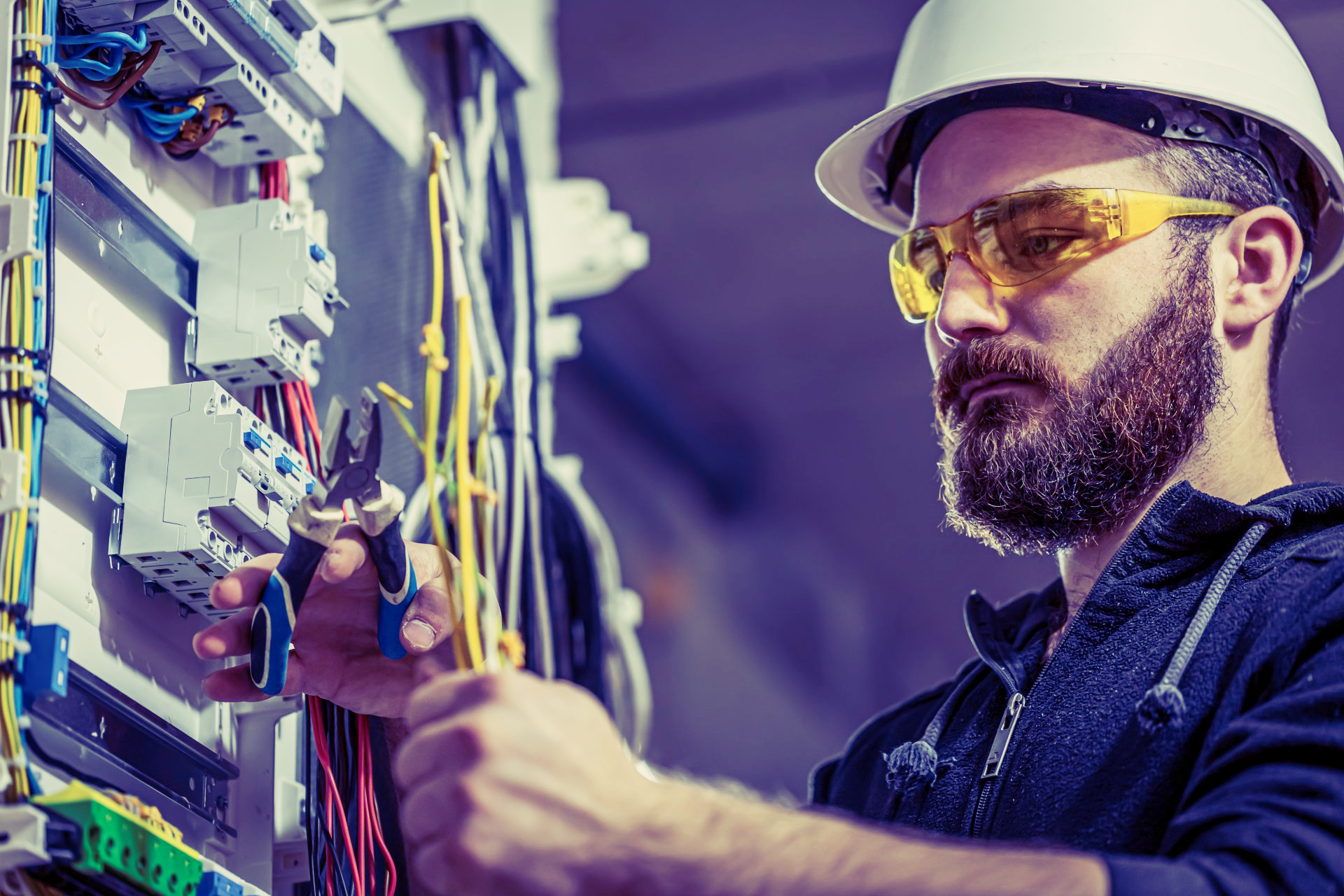 Um eletricista usando capacete e óculos de segurança está trabalhando em uma caixa elétrica.