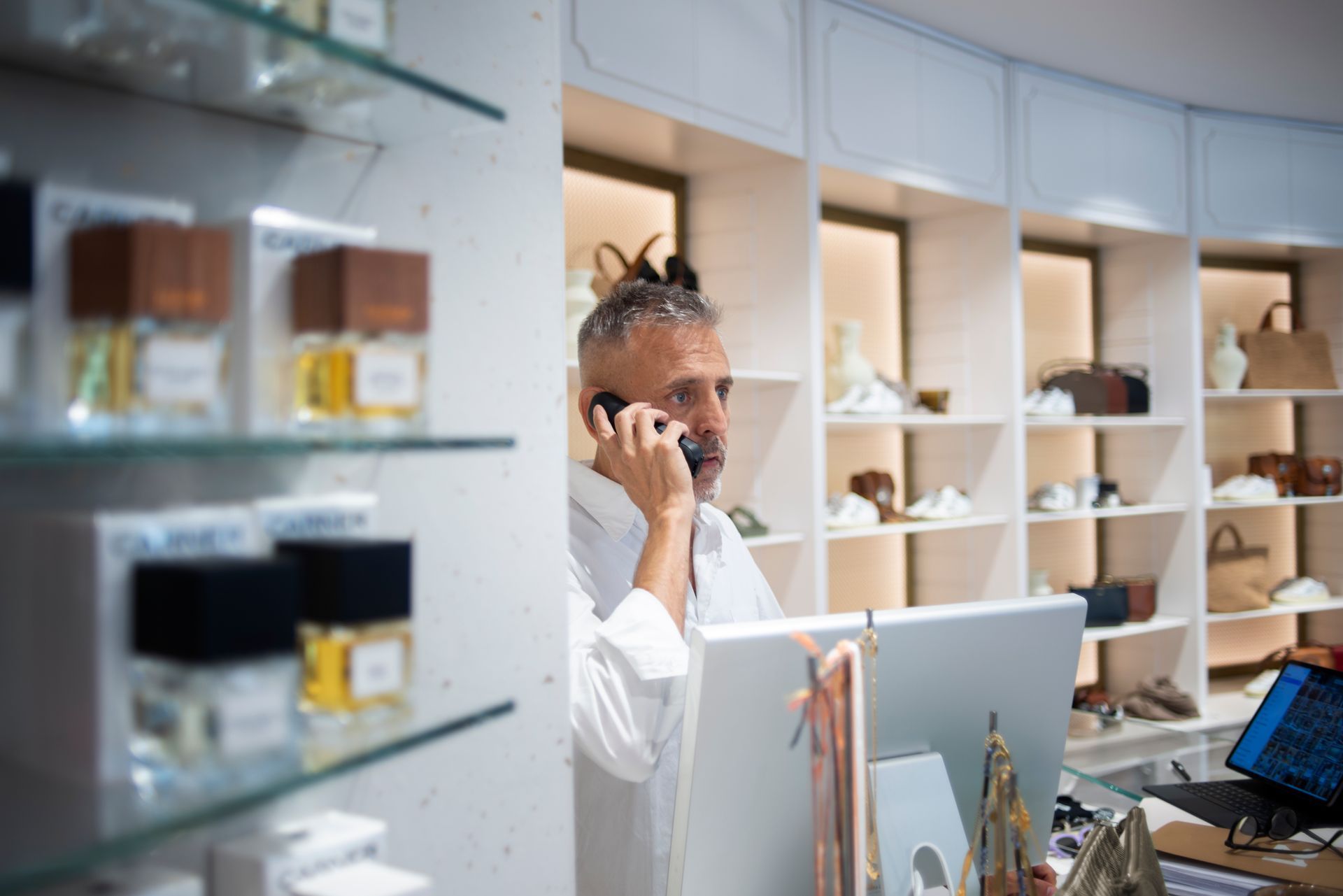 Um homem está falando ao celular em frente a um computador em uma loja.
