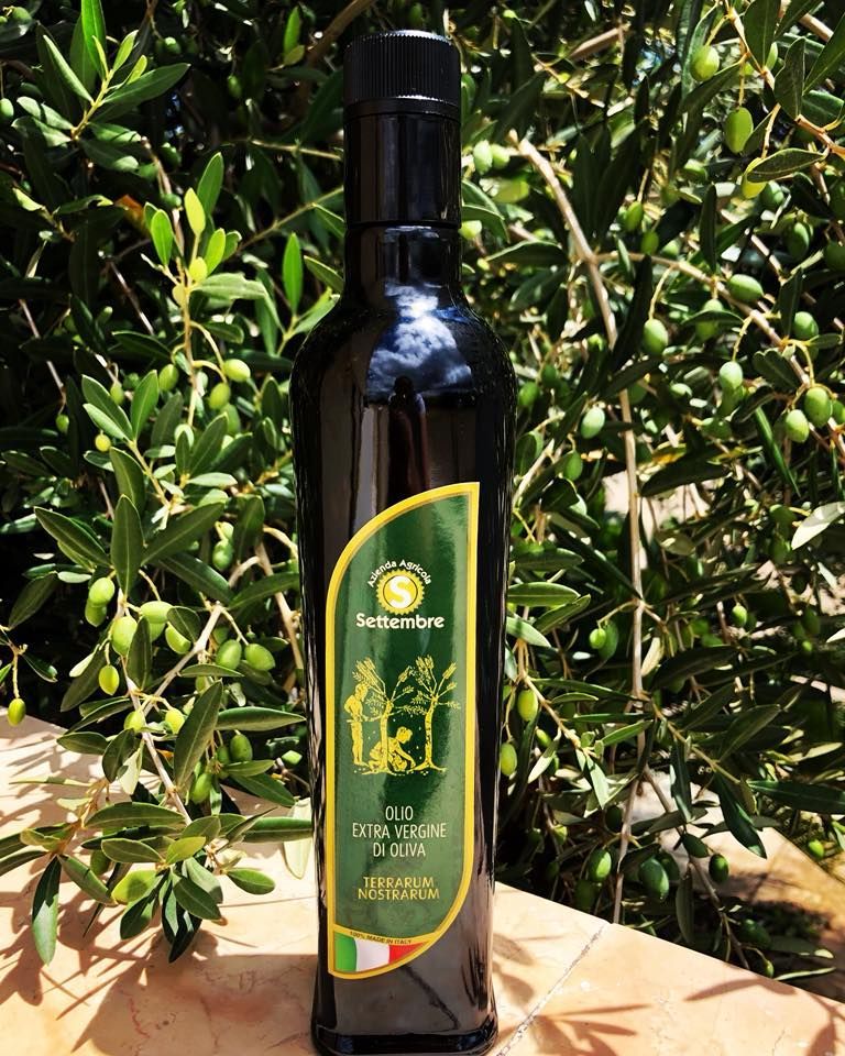 Bottiglia di olio d'oliva con etichetta verde e oro, davanti a rami di ulivo.