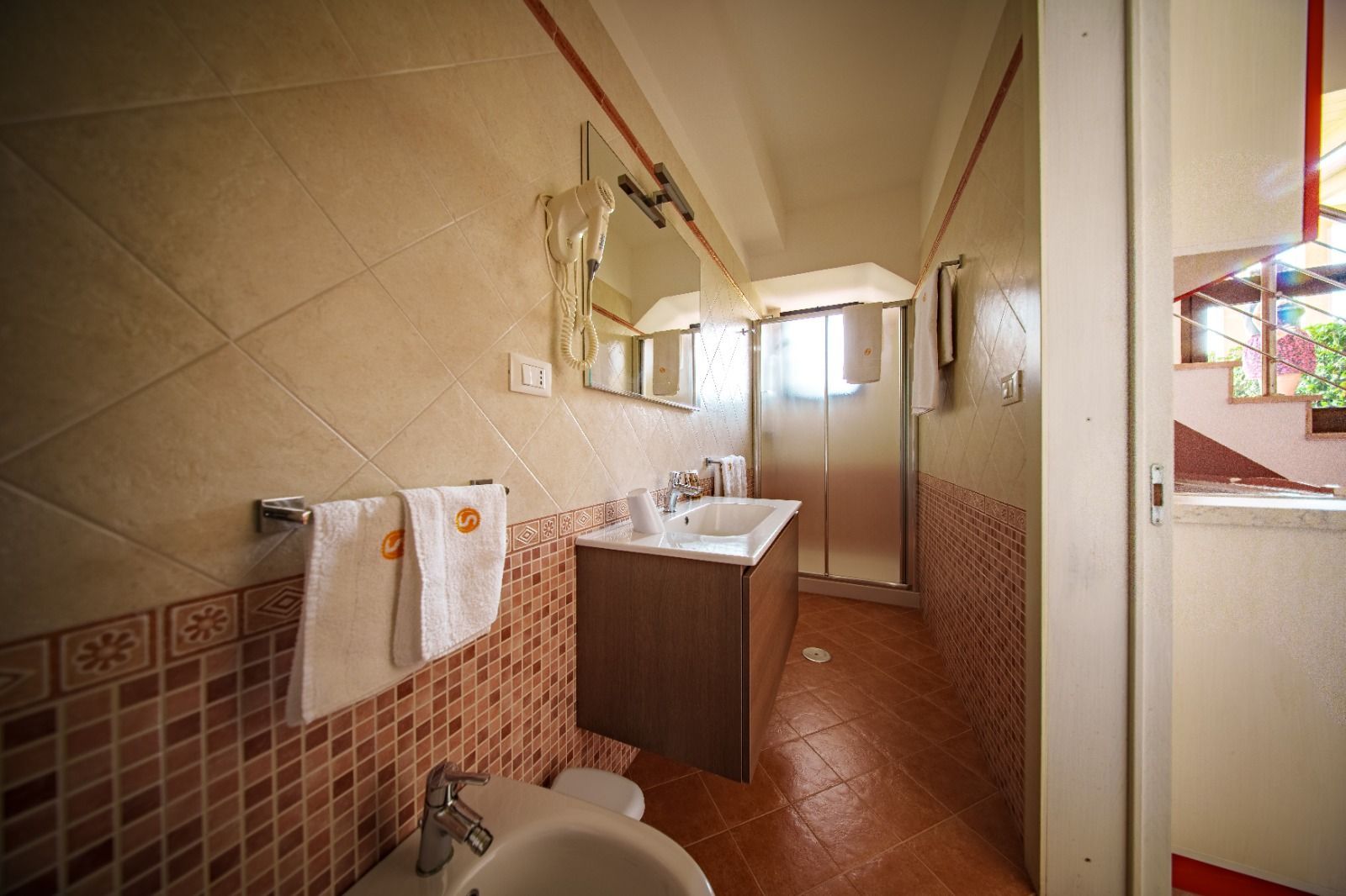 Bagno con piastrelle beige e marroni, lavandino, doccia e asciugamani.