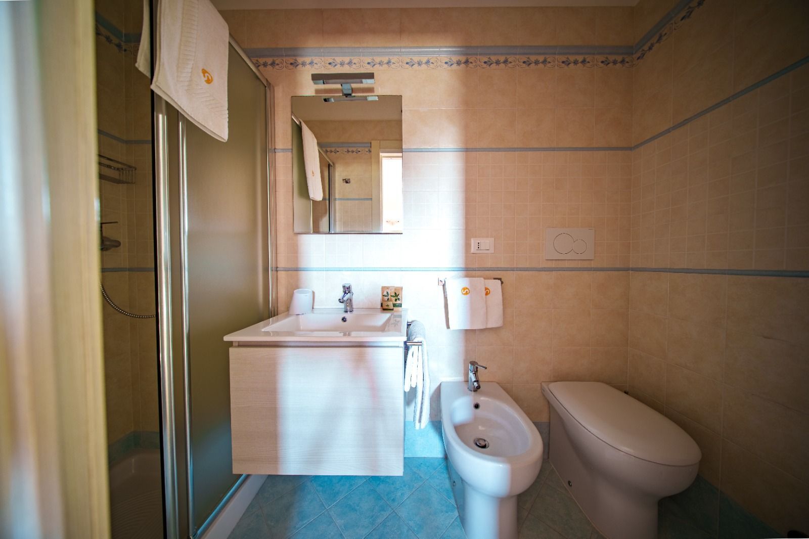 Bagno con lavandino, WC, bidet e box doccia. Pareti beige, porta della doccia in vetro smerigliato e uno specchio sopra il lavandino.