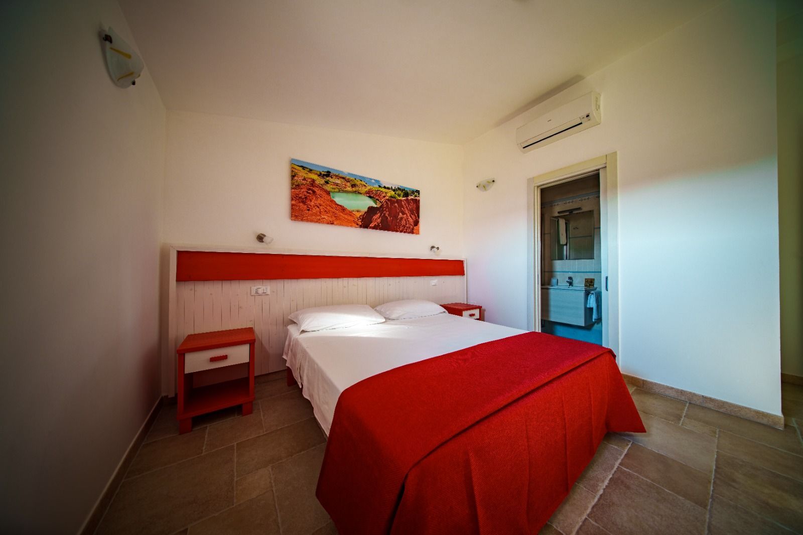 Camera da letto con pareti bianche, dettagli rossi e un letto matrimoniale con copriletto rosso.