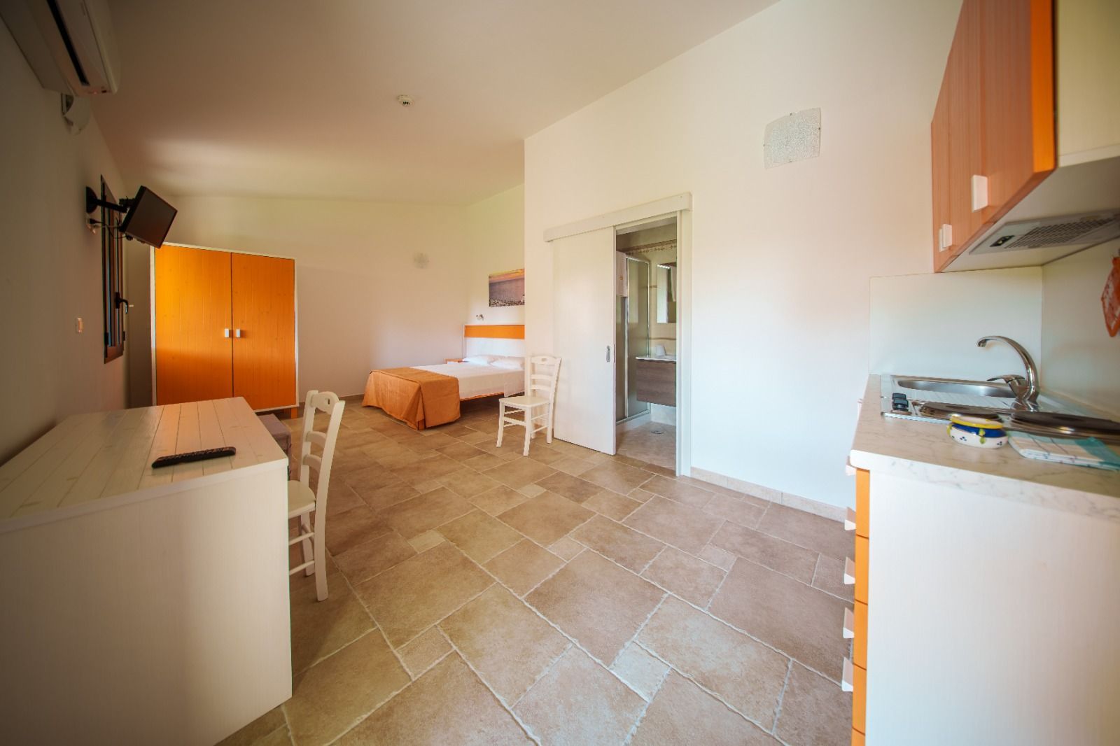 Monolocale con angolo cottura, letto, scrivania, armadio e porta aperta sul bagno.