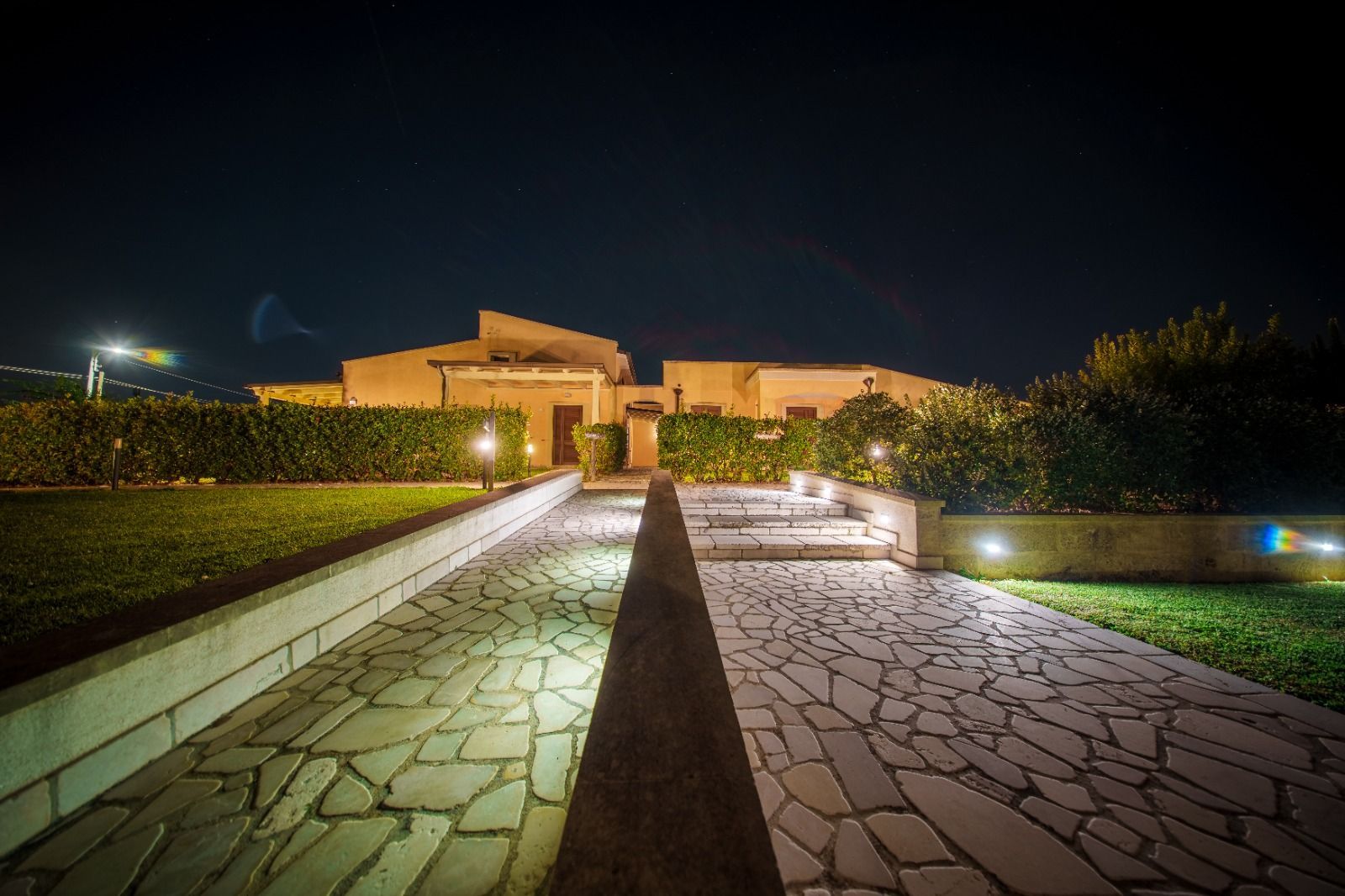 Sentiero in pietra che conduce a una casa di notte, illuminato dalle luci del giardino e da un cielo scuro.